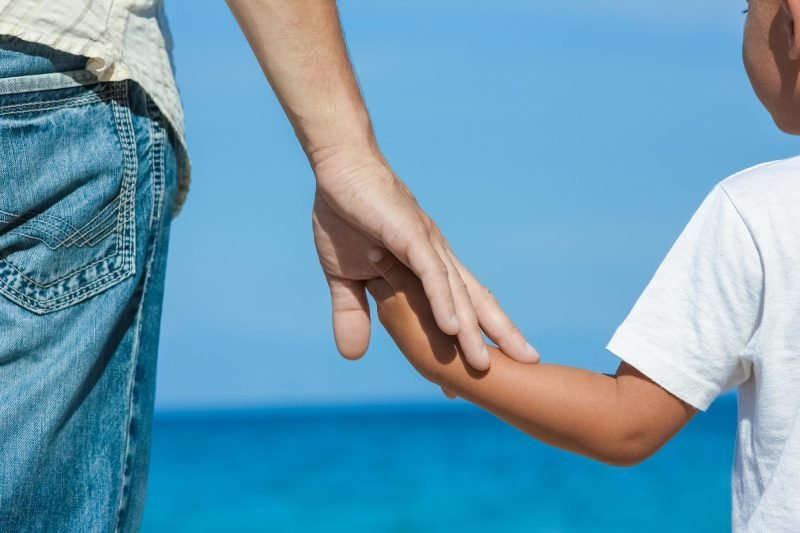 Happy dad holds the hand of a child by the greek sea in nature