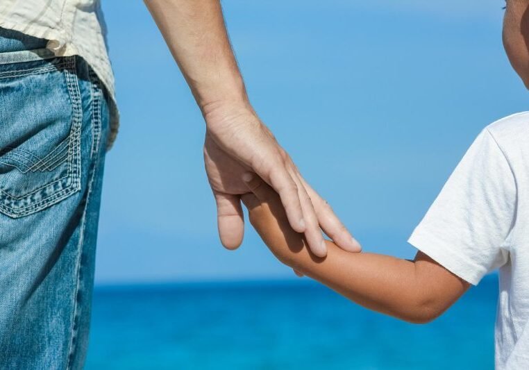 Happy dad holds the hand of a child by the greek sea in nature